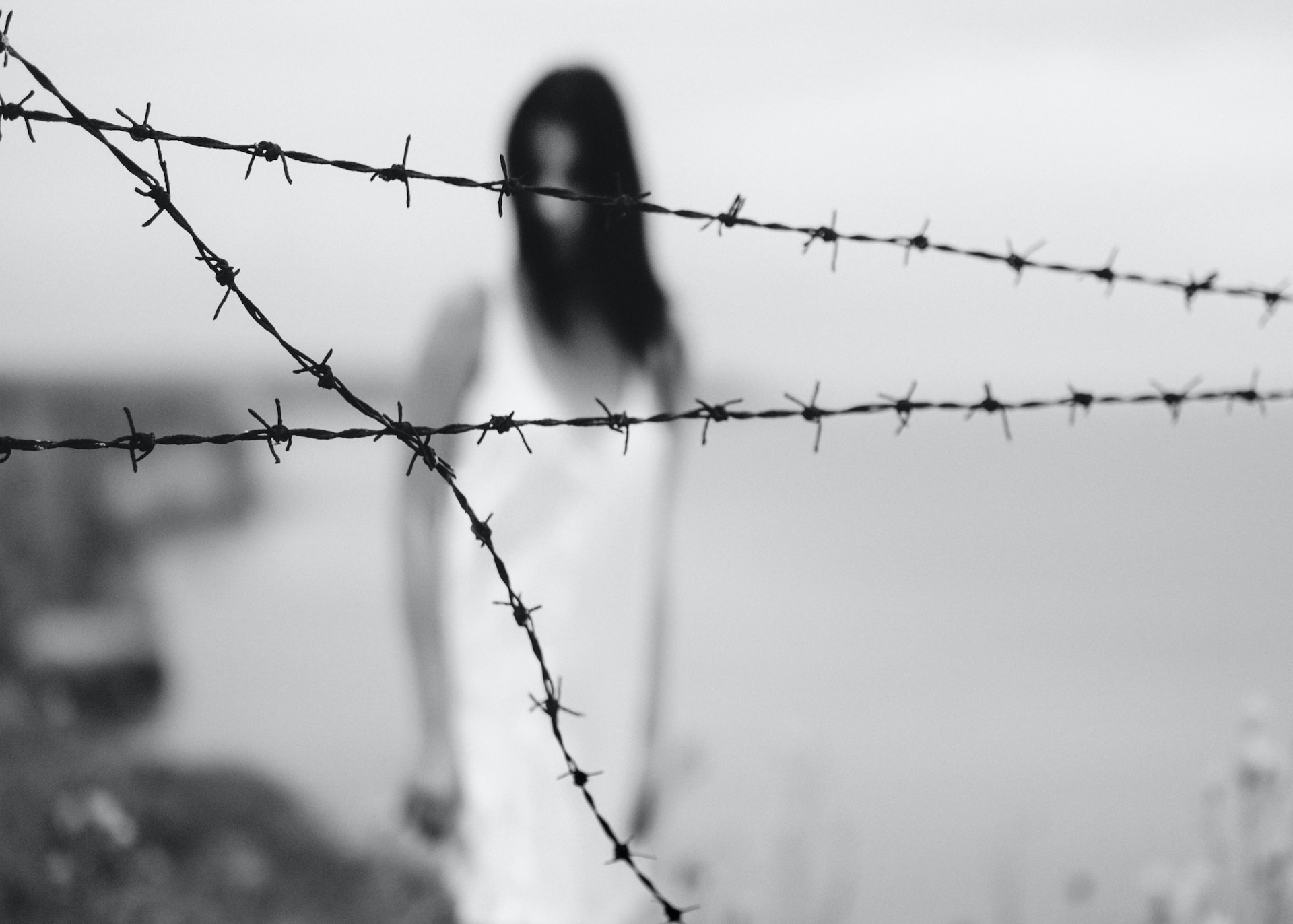 Blurred image of a distant woman through barbed wire